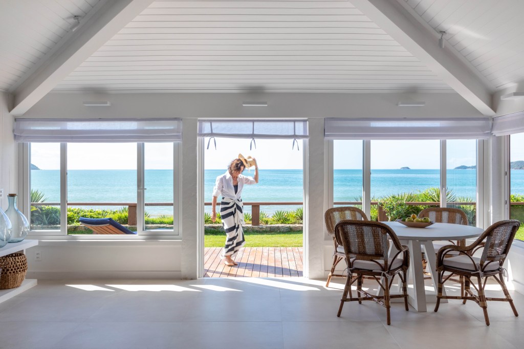 Venezianas azuis na varanda marcam esta casa de praia inspirada na Grécia. Projeto de Brise Arquitetura. Na foto, sala de jantar com vista para o mar.