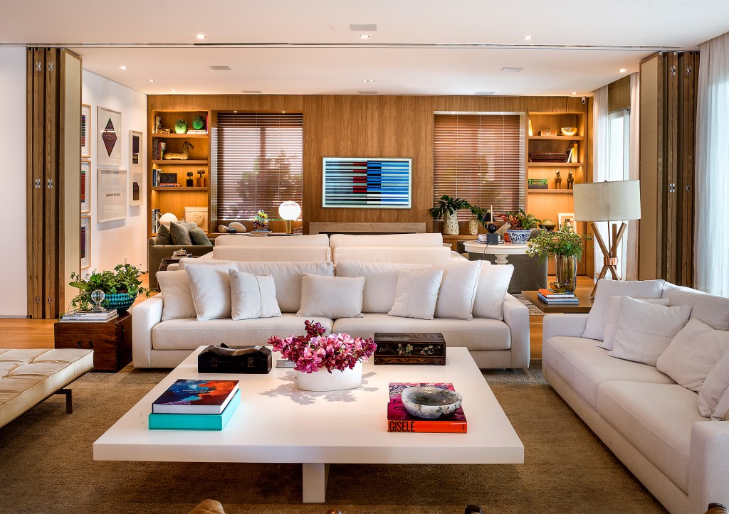 paola-ribeiro-apartamento-810-m2-repleto-arte-credito-romulo-fialdini (19) Paola Ribeiro assina apartamento de 810 m² repleto de arte. Na foto, sala de estar com sofás brancos, parede de madeira e quadros.