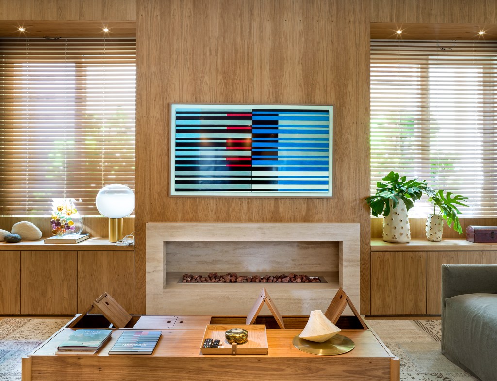 paola-ribeiro-apartamento-810-m2-repleto-arte-credito-romulo-fialdini (7) Paola Ribeiro assina apartamento de 810 m² repleto de arte. Na foto, sala de estar com quadro, lareira e parede de madeira.