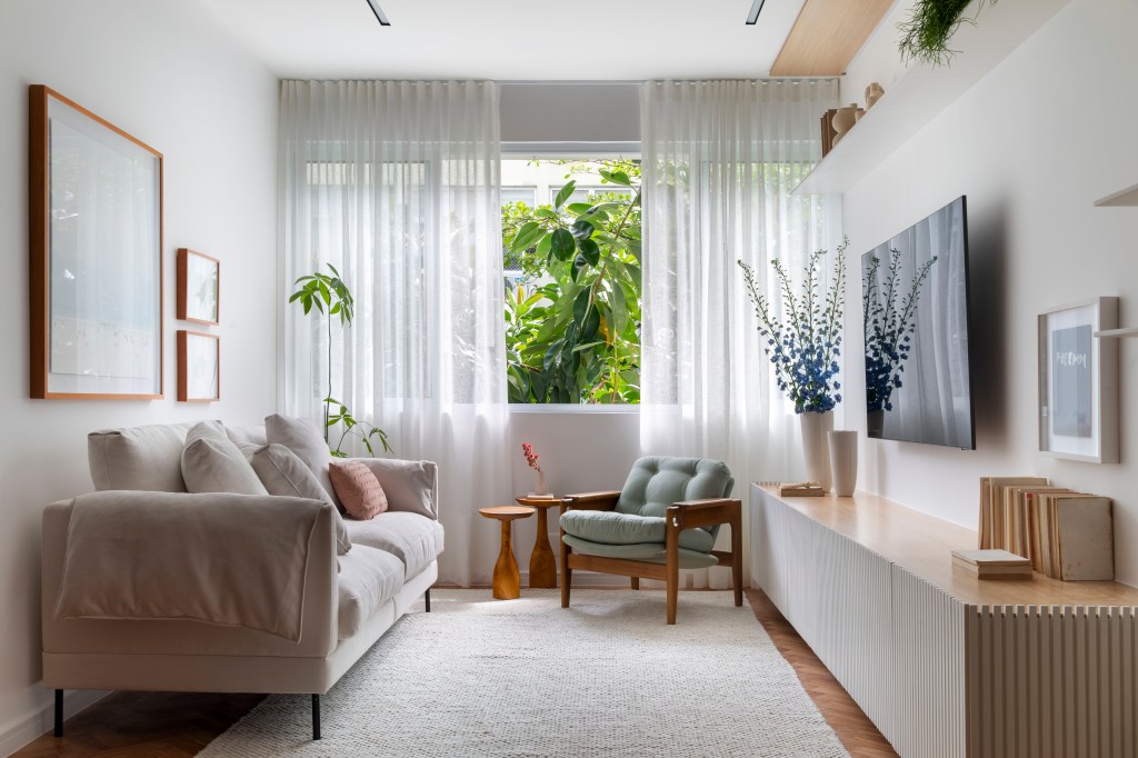 Apartamento de 110 m² ganha décor aconchegante com clima carioca. Projeto de Rafael Ramos. Na foto, sala de estar com aparador ripado e quartos.