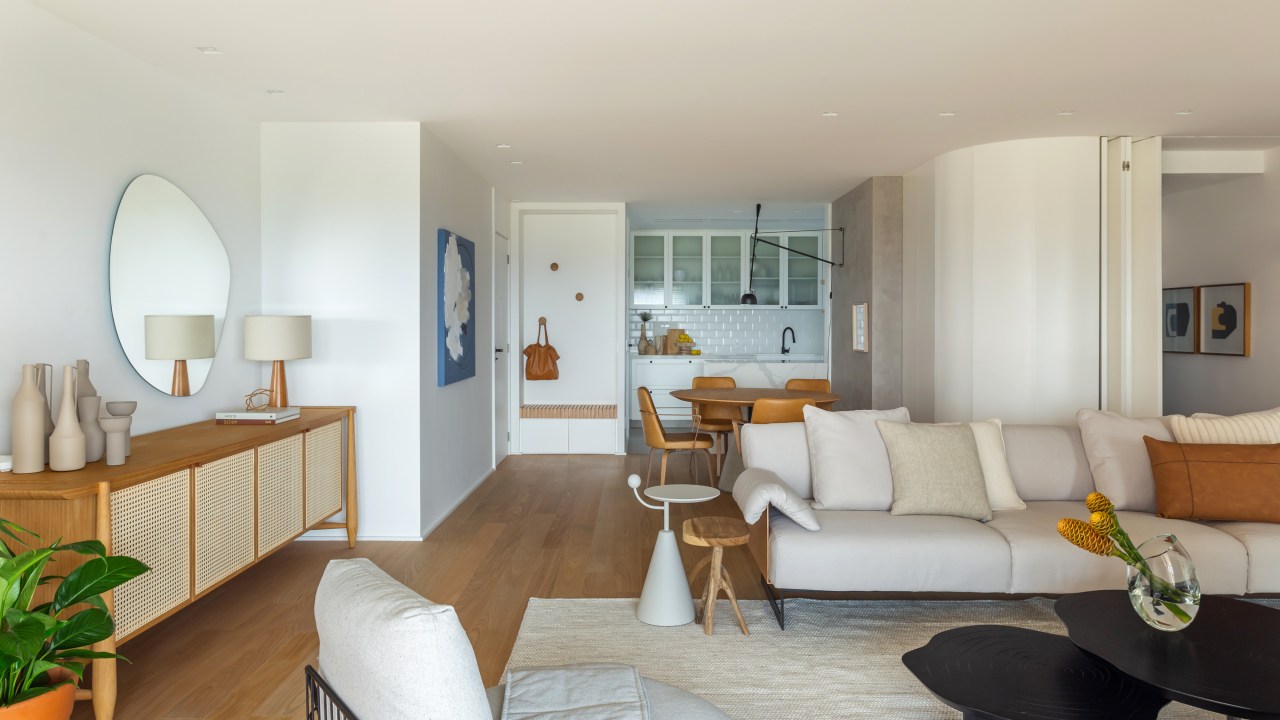 Apê na Barra da Tijuca ganha décor minimalista, mas muito aconchegante. Projeto de A+G Arquitetura, Na foto, sala de estar integrada com cozinha com decor claro, aparador e sofás.