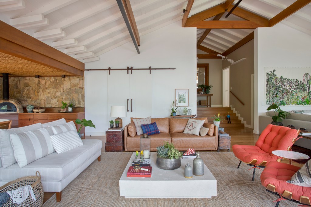 Suíte de casa de campo fica em bangalô suspenso no meio da natureza. Projeto de Escala Arquitetura. Na foto, sala de estar com escada, parede de pedra, varanda com churrasqueira.