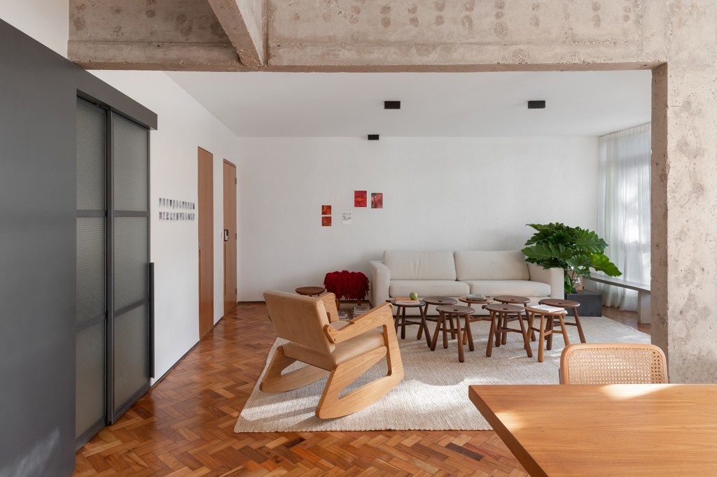Apê brutalista em Brasília mescla cobogó, ladrilho e concreto no décor. Projeto de Maria Araujo Arquitetura, Na foto, sala de estar com tapete, piso de madeira e painel na parede.