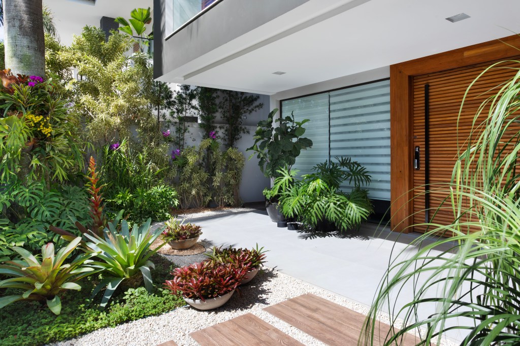 jardim-tropical-mix-folhagens-texturas-vegetacao-horto-girassol-credito-mca-estudio (5) Jardim tropical traz mix de folhagens, texturas e vegetação. Projeto de Horto Girassol. Na foto, jardim com vasos, caminho e pedras. Fachada e porta de entrada.