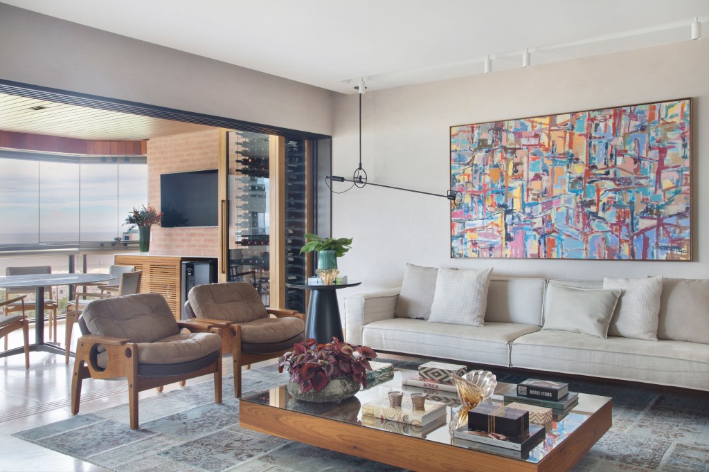 materiais-nobres-paleta-atemporal-marcam-apartamento-280-m2-studio-0210-credito-mca-estudio (13) Materiais nobres e paleta atemporal marcam este apartamento de 280 m². Projeto de Studio 021. Na foto, varanda com vista para o mar e sofás. Adega e TV. Sala de estar com quadro colorido.