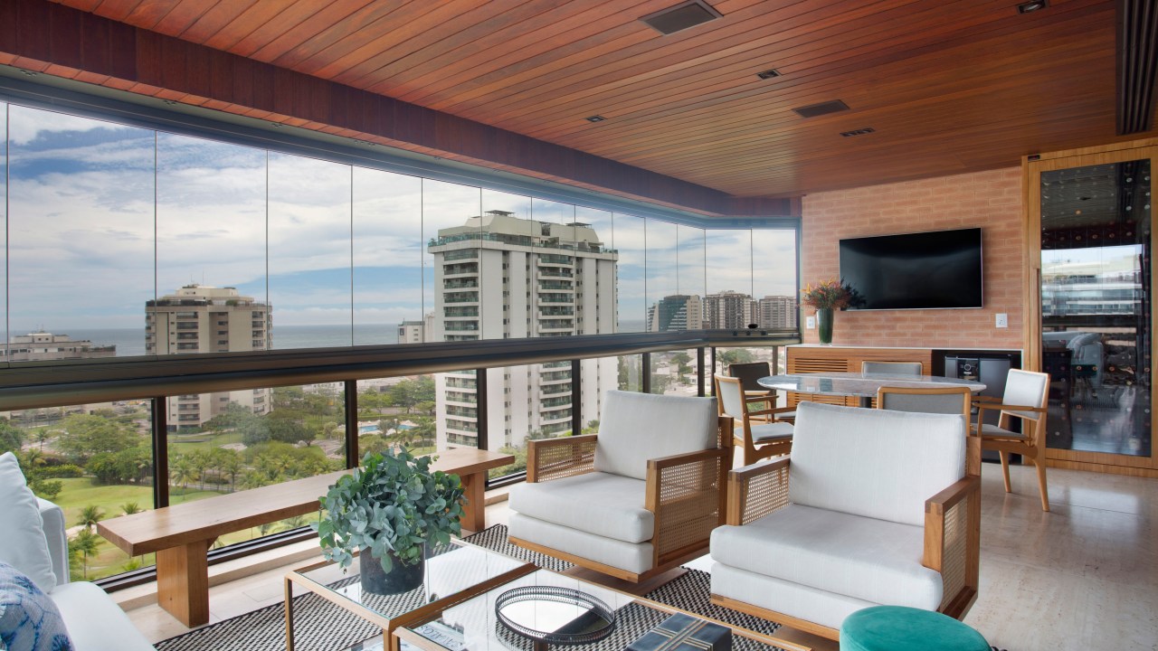 Materiais nobres e paleta atemporal marcam este apartamento de 280 m². Projeto de Studio 021. Na foto, varanda com vista para o mar e sofás. Adega e TV.