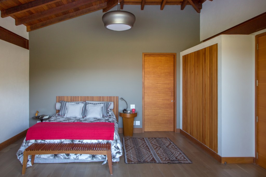 Casa na montanha possui vista espetacular para a Serra das Araras. Projeto de Andrea Chicharo. Na foto, quarto de casal com armário ripado e teto de madeira.