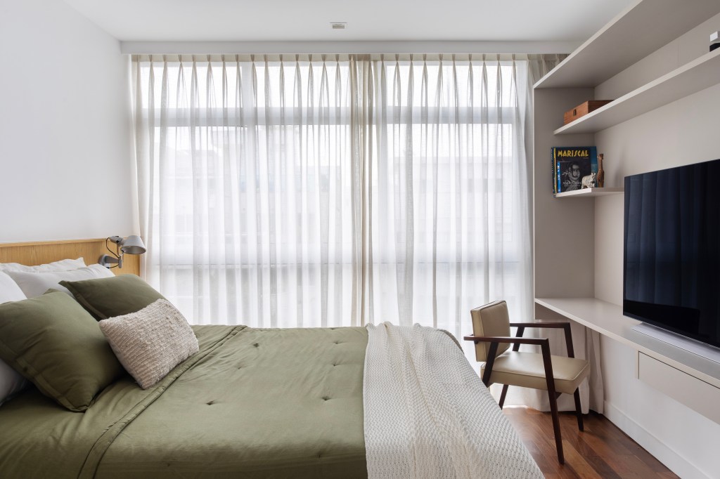 Paredes brancas, piso de madeira e armários verdes marcam apê de 280 m². Projeto Beta Arquitetura. Na foto, quarto de casal com tv e home office.