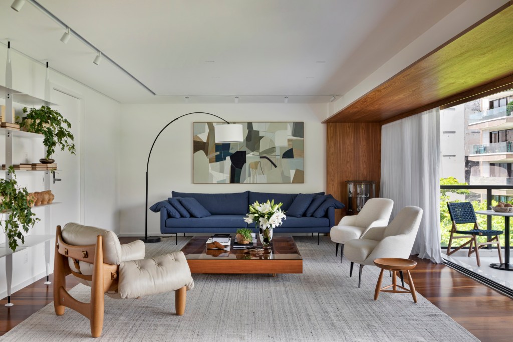 Com ampla varanda, apê de 200 m² tem décor inspirada no bairro do Leblon. Projeto de João Panaggio. Na foto, sala de estar com sofá azul e varanda com vista para as árvores.