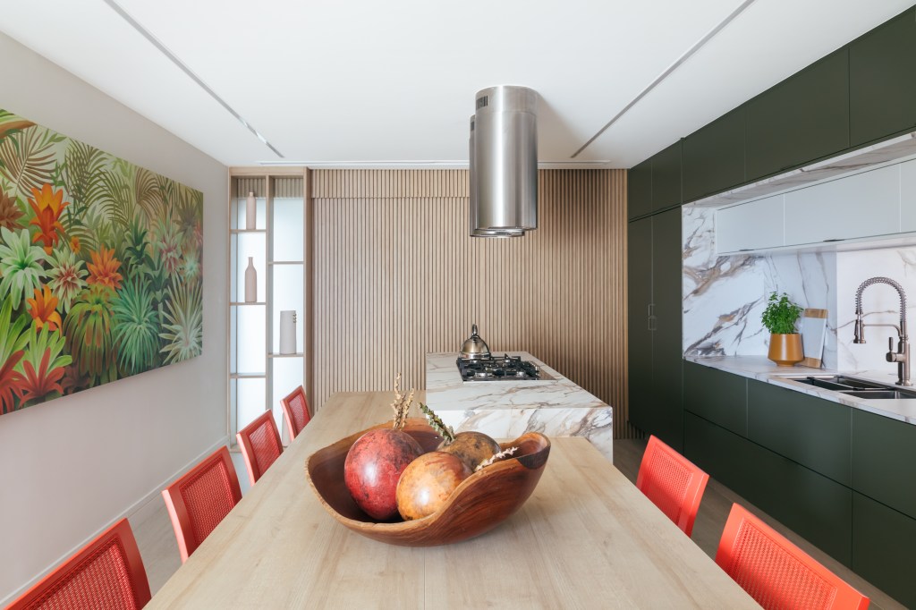 Apê de 350 m² tem vista para o mar, sauna e canto especial para charutos. Projeto de Vivian Reimers. Na foto, cozinha com marcenaria verde, cadeiras vermelhas e ilha.