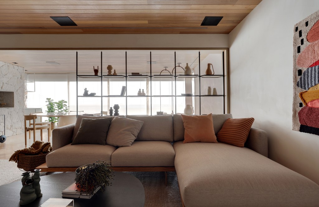 Com cara de casa, apê de 150 m² une integração ao aconchego da madeira. Projeto Bárbara Dundes. Na foto, sala com estante vazada. Quadro e sofá.