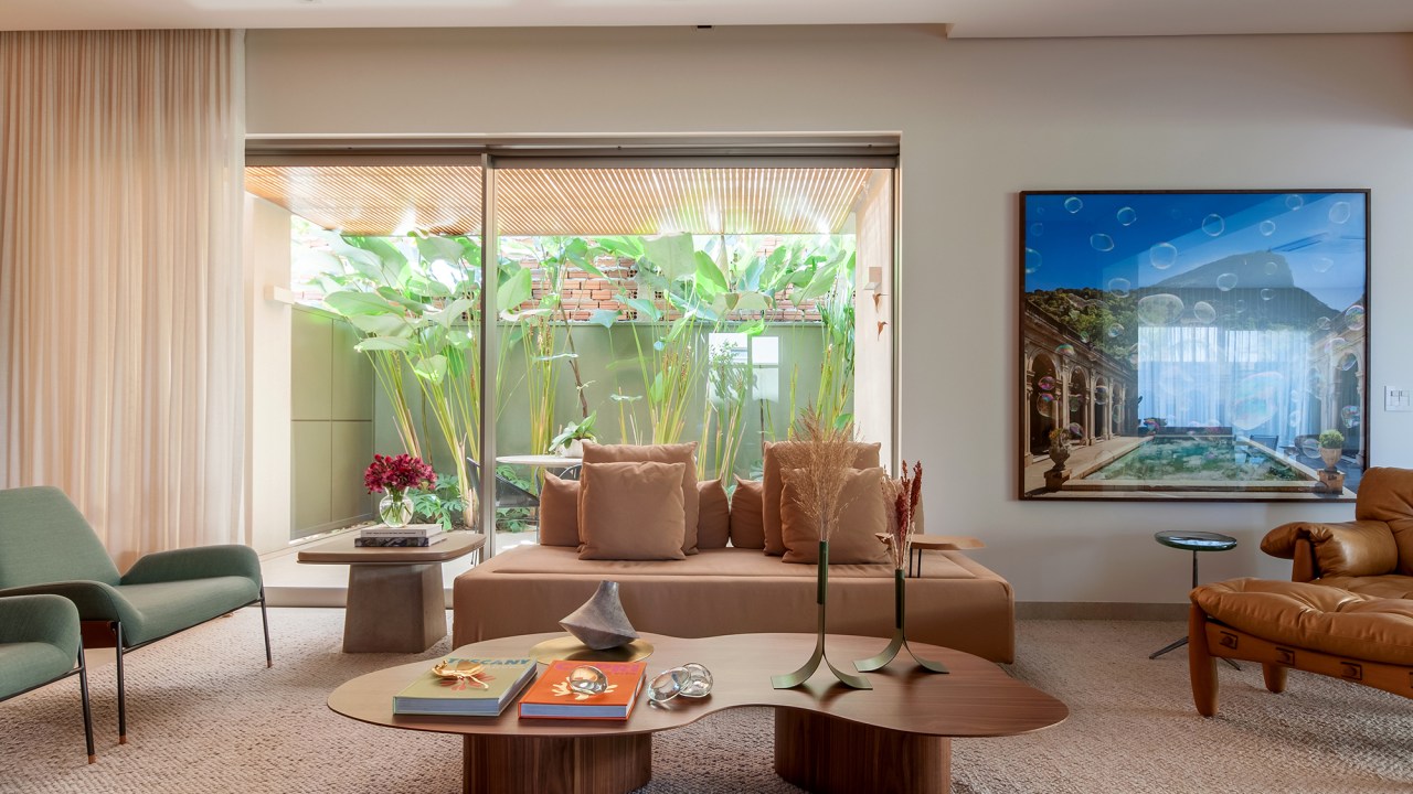 Construída do zero, casa une ambientes integrados e design nacional. Projeto de Paiva e Passarini Arquitetura. Na foto, sala de estar com painel de madeira e quadros.