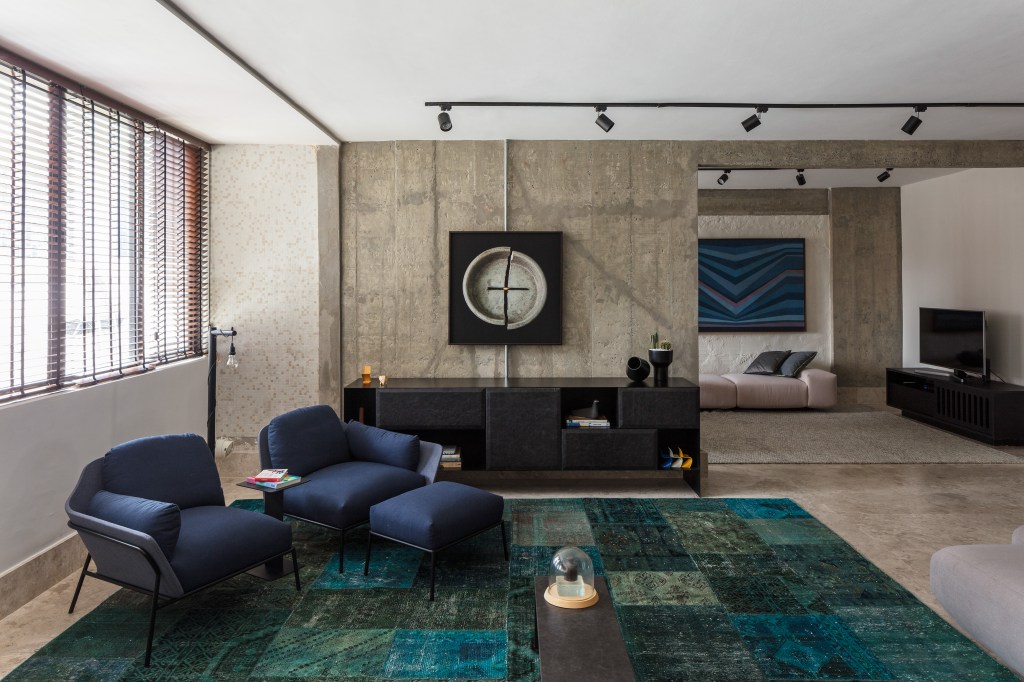 José Navarro assina apartamento de 210 m² no Conjunto Nacional, em SP. Na foto, sala de estar com parede concreto, tapete e poltronas azuis.