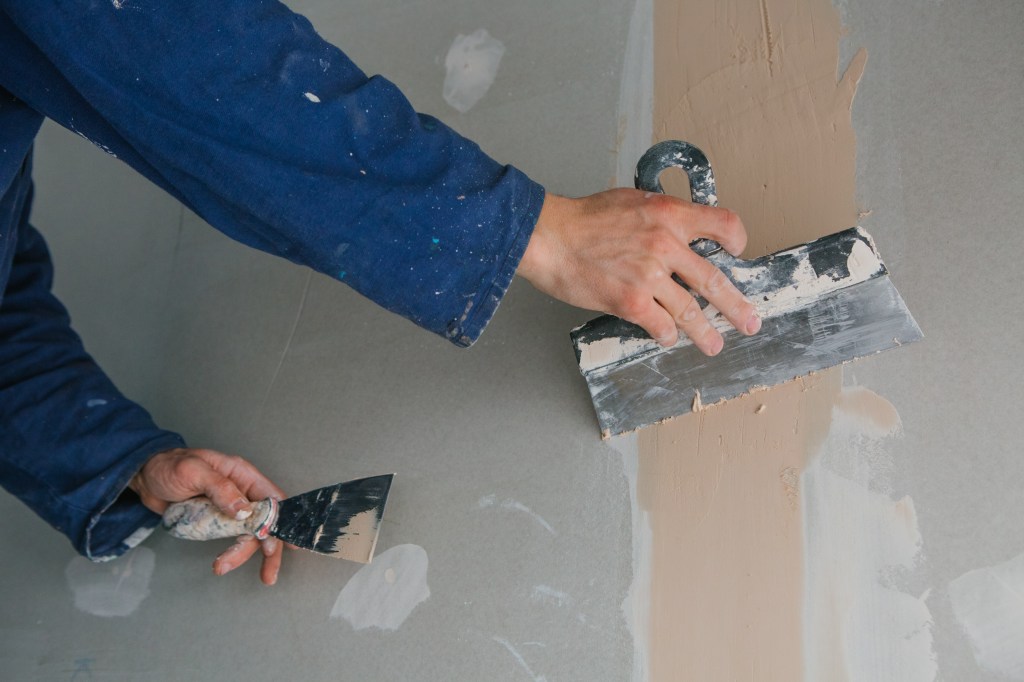 plasterer works plastering two trowels plasterboard blue uniform Aplicação de massa corrida