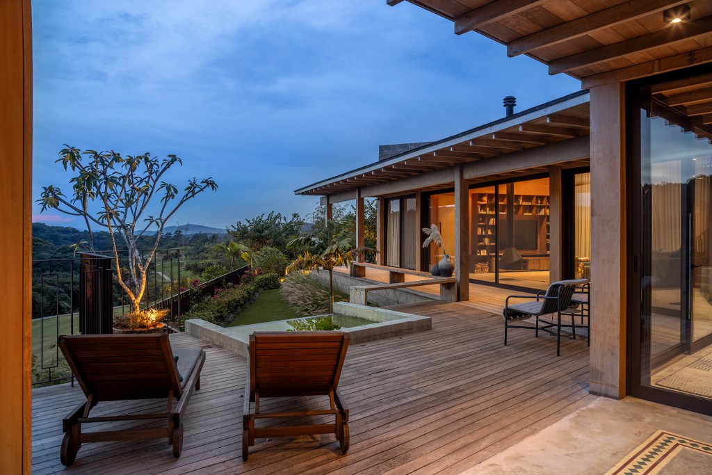 Casa sustentável e integrada à natureza fica em frente ao campo de golfe. Projeto de In House Arquitetura. Na foto, varanda com banco e vista para jardim. Deque e banheira.