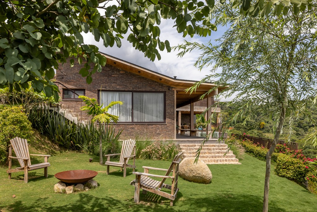 Casa sustentável e integrada à natureza fica em frente ao campo de golfe. Projeto de In House Arquitetura. Na foto, fachadas dos fundos, fogo de chão e jardim.