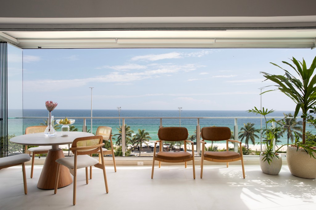 De frente para o mar, um apartamento ideal para curtir a aposentadoria. Projeto de Rafael Ramos. Na foto, varanda com mesa, cadeiras e plantas.