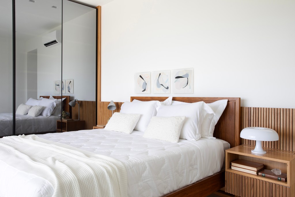 De frente para o mar, um apartamento ideal para curtir a aposentadoria. Projeto de Rafael Ramos. Na foto, quarto de casal com quadros e cabeceira de madeira.