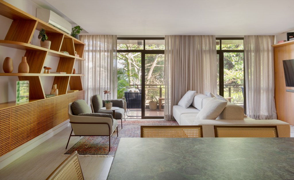 A madeira é a protagonista deste apartamento de 117 m² na Gávea. Projeto de Mariana Monnerat, Na foto, sala com estante assimétrica de madeira. Varanda e sofá ilha.