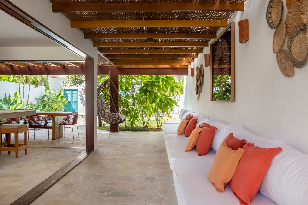 Refúgio tropical: casa em Trancoso ganha quarto de hóspedes na edícula. Projeto Conrado Ceravolo. Na foto, varanda com sofá, teto de palha e jardim.