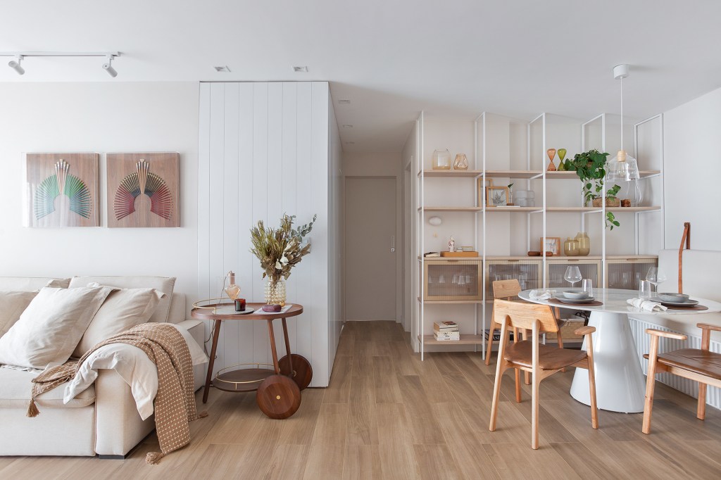 Tons suaves, brises na sala e mistura de pisos marcam apê de 93 m². Projeto de Manoela Fleck. Na foto, sala com sofá branco, quadros e mesa. Sala de jantar com mesa redonda.