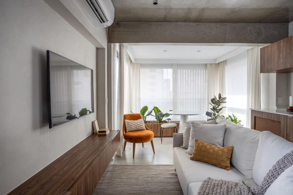 jp-image.com Wabi-sabi norteia a decoração de apartamento de apenas 48 m². Projeto de Carolina Gava. Na foto. sala de estar com sofá branco, cozinha e tv,