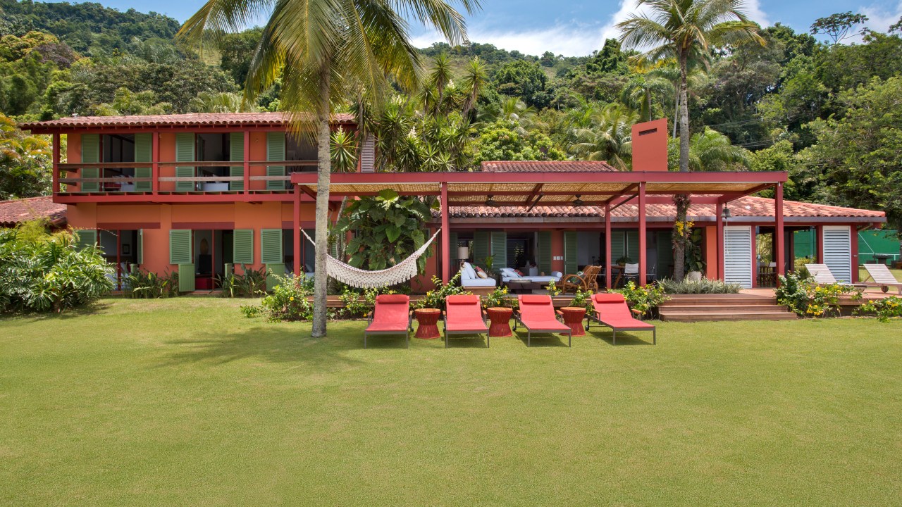 Casa com vista para o mar e nove suítes ganha nova varanda na reforma. Projeto de Escala Arquitetura. Na foto, fachada da casa com jardim e varanda.