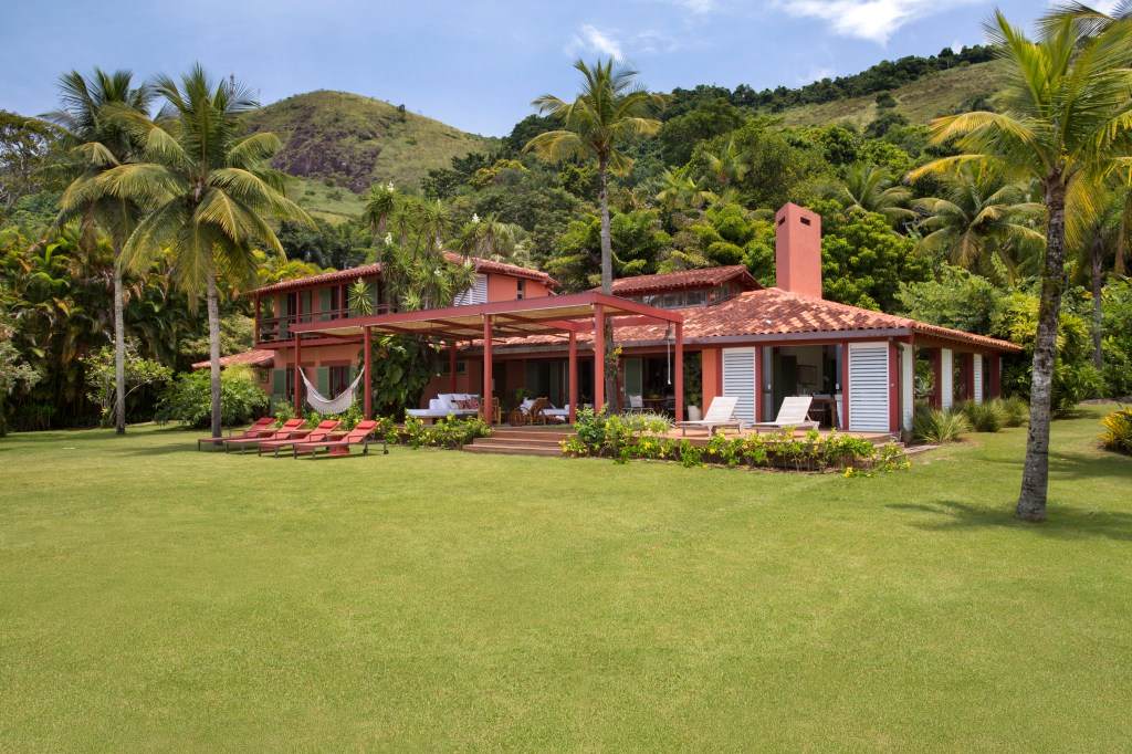 Casa com vista para o mar e nove suítes ganha nova varanda na reforma. Projeto de Escala Arquitetura. Na foto, fachada da casa com jardim e varanda.