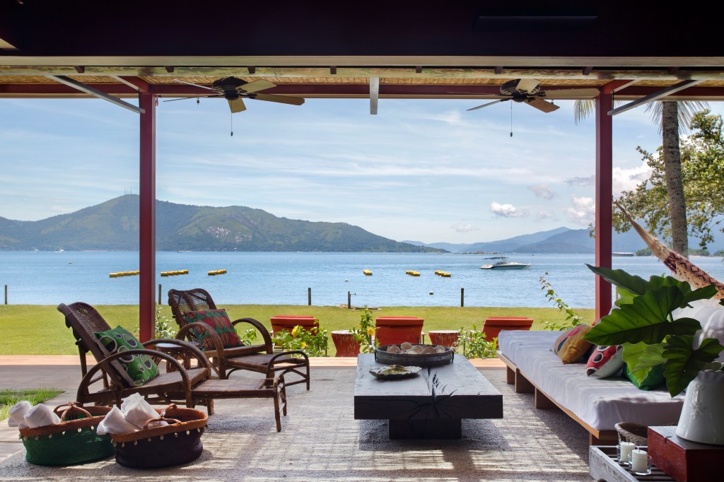 Casa com vista para o mar e nove suítes ganha nova varanda na reforma. Projeto de Escala Arquitetura. Na foto, varanda com sofá, rede e vista para o mar.