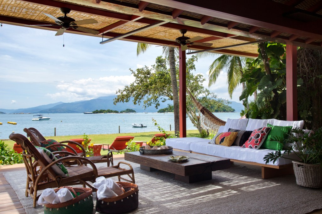 Casa com vista para o mar e nove suítes ganha nova varanda na reforma. Projeto de Escala Arquitetura. Na foto, varanda com sofá, rede e vista para o mar.