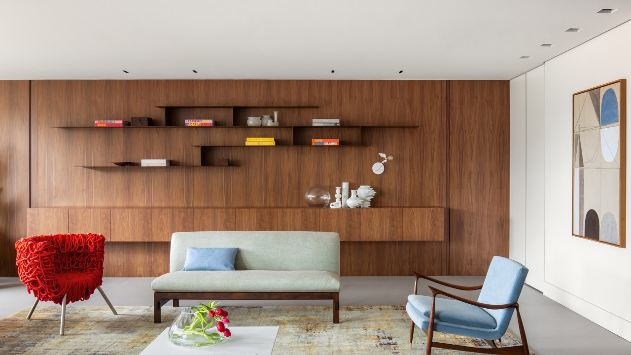 Madeira escura e tons sóbrios dão ar masculino a apê de 245 m². Projeto de Nildo José Arquitetura. Na foto, sala de estar com parede de madeira, tapete e poltronas.