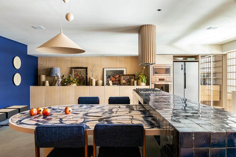 <b>Mandril Arquitetura - Cozinha Torno</b>. Os sócios Bruno Reis e Helena Kallas propõem uma cozinha e sala de almoço para encontros em família. Com 55 m², o projeto se vale da experiência da dupla de criar, especialmente para a mostra, a coleção de vasos e bases de luminárias exposta no ambiente. Modeladas em torno, instrumento milenar que convida à atenção plena durante a atividade manual, as peças prestam homenagem à matéria-prima e sua história. Os arquitetos também desenharam os azulejos artesanais que compõem o tampo da mesa e empregam um pigmento azul 100% natural.