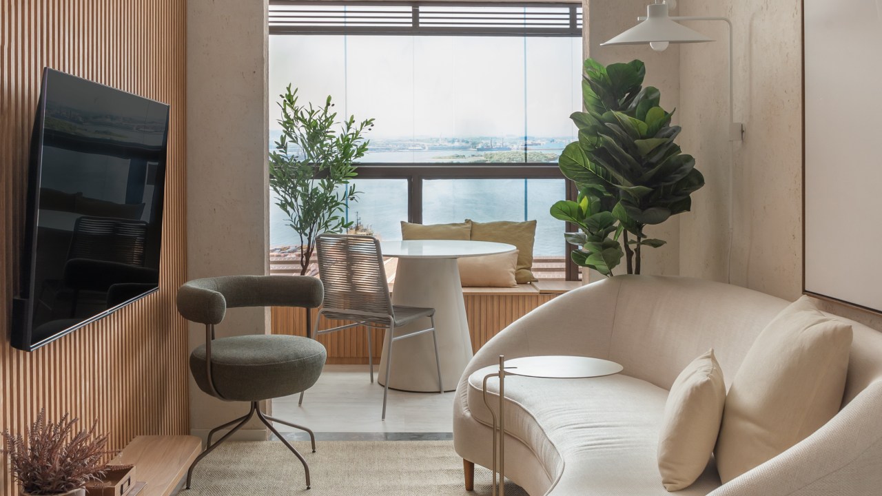 Tons claros e arenosos trazem aconchego a este apartamento de 49 m². Projeto de Leandro Neves. Na foto, sala com varanda integrada, sofá curvo e parede ripada.