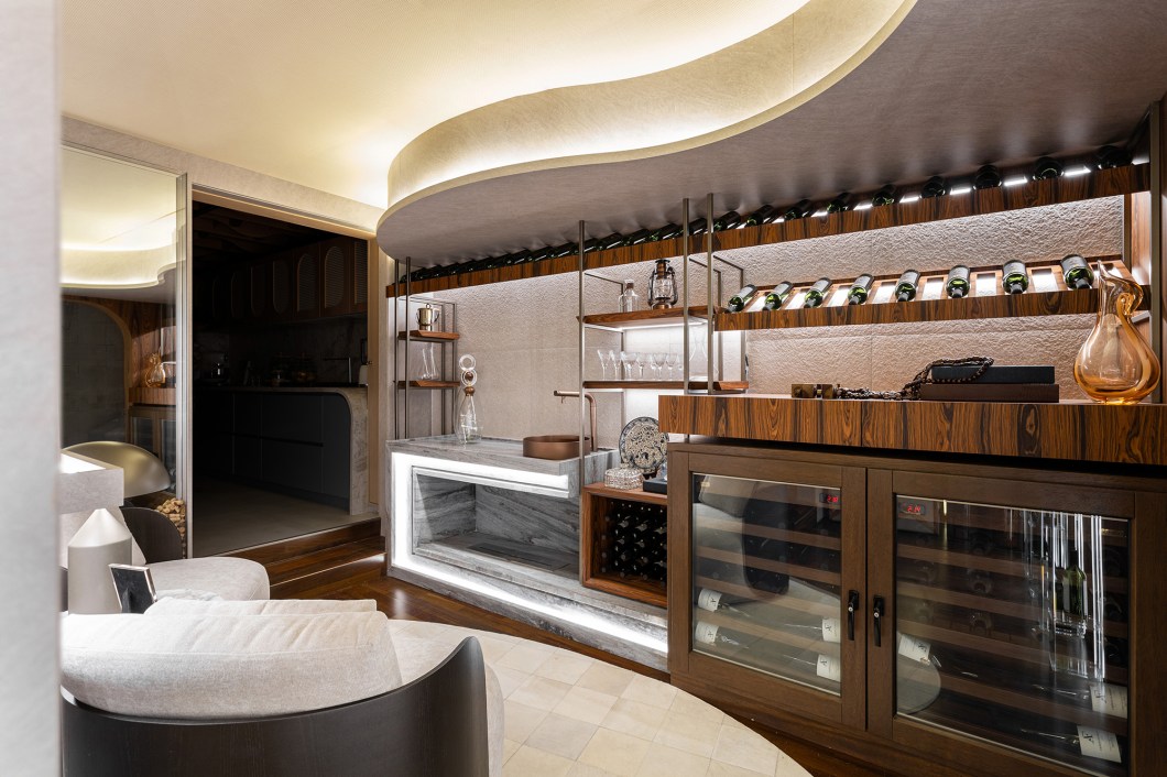 <b>Janaina Marques e Camila Kubota - Adega Residencial. </b>Além de ser uma adega funcional, este espaço proporciona uma experiência imersiva para os apreciadores da enologia. Com uma área climatizada que segue todas as exigências técnicas para a conservação dos vinhos, o ambiente inclui uma parede dedicada à exposição de rótulos especiais, uma bancada equipada com cuba e apoio para o manuseio das garrafas, e poltronas para degustação das bebidas. As arquitetas utilizam a marcenaria para criar um fluxo que guia o visitante até o ápice do projeto, onde desenham uma tela tensionada com padrões que remetem aos formatos das garrafas. Na lateral, o painel com prateleiras de vidro destaca ainda mais os rótulos especiais. <b>Janaina Marques e Camila Kubota - Adega Residencial. </b>Além de ser uma adega funcional, este espaço proporciona uma experiência imersiva para os apreciadores da enologia. Com uma área climatizada que segue todas as exigências técnicas para a conservação dos vinhos, o ambiente inclui uma parede dedicada à exposição de rótulos especiais, uma bancada equipada com cuba e apoio para o manuseio das garrafas, e poltronas para degustação das bebidas. As arquitetas utilizam a marcenaria para criar um fluxo que guia o visitante até o ápice do projeto, onde desenham uma tela tensionada com padrões que remetem aos formatos das garrafas. Na lateral, o painel com prateleiras de vidro destaca ainda mais os rótulos especiais.